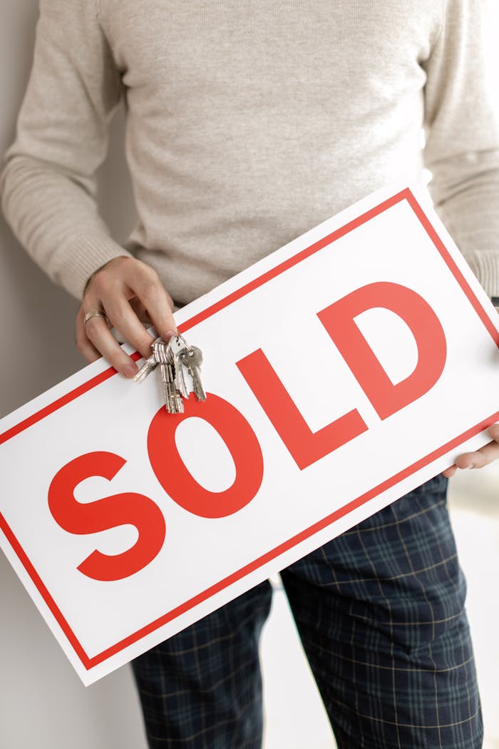 Close-up of a realtor holding a sold sign and keys, symbolizing successful property sale.